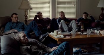 Movie still from “Foxcatcher” (2014), directed by Bennett Miller – A group of men sitting on a couch in a living room; Wide shot, High angle