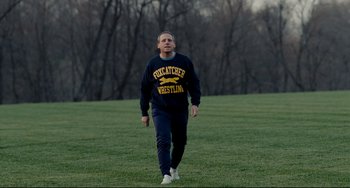 Movie still from “Foxcatcher” (2014), directed by Bennett Miller – A man walking across a lush green field; Medium shot, Low angle