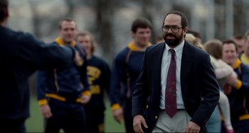 Movie still from “Foxcatcher” (2014), directed by Bennett Miller – A man in a suit and tie walking with other men; Medium shot, Over the shoulder angle