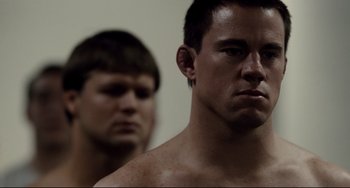 Movie still from “Foxcatcher” (2014), directed by Bennett Miller – A man standing next to another man in front of a wall; Close Up shot, Over the shoulder angle