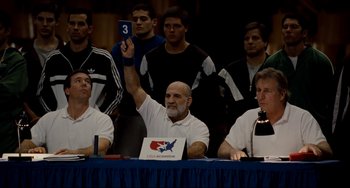Movie still from “Foxcatcher” (2014), directed by Bennett Miller – A group of men sitting at a table holding up a card; Medium shot, Over the shoulder angle
