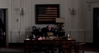 Movie still from “Foxcatcher” (2014), directed by Bennett Miller – A man sitting at a desk in front of an american flag on the wall; Wide shot, High angle