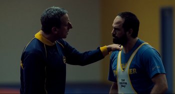 Movie still from “Foxcatcher” (2014), directed by Bennett Miller – Two men are wrestling one of them has his hand on the other's shoulder; Medium shot, Over the shoulder angle