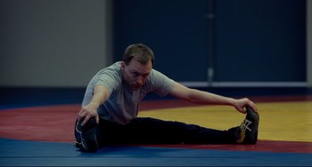 Movie still from “Foxcatcher” (2014), directed by Bennett Miller – A man stretching on the ground in a gym; Medium shot, High angle