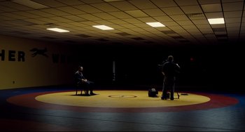 Movie still from “Foxcatcher” (2014), directed by Bennett Miller – Two men sitting on chairs in a wrestling ring; Extreme Wide shot, Over the shoulder angle