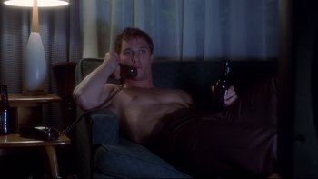 Movie still from “Frailty” (2001), directed by Bill Paxton – A man laying on a couch talking on the phone and holding a beer; Medium shot, Low angle
