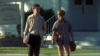 Movie still from “Frailty” (2001), directed by Bill Paxton – Two young men walking on the sidewalk in front of a house; Medium shot, Low angle