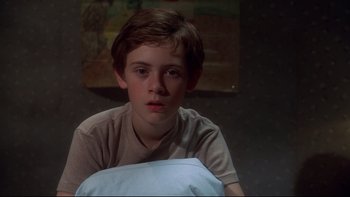 Movie still from “Frailty” (2001), directed by Bill Paxton – A young boy sitting in a chair in a dark room; Close Up shot, Over the shoulder angle