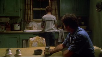 Movie still from “Frailty” (2001), directed by Bill Paxton – A man sitting at a table in front of a kitchen sink; Medium shot, Low angle