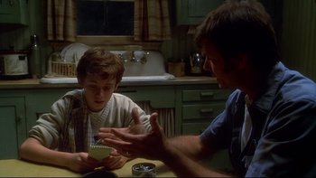 Movie still from “Frailty” (2001), directed by Bill Paxton – Two people sitting at a table in front of one another; Medium shot, Over the shoulder angle