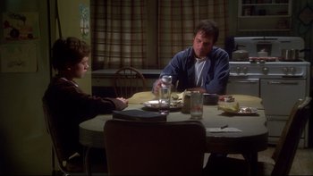 Movie still from “Frailty” (2001), directed by Bill Paxton – Two people sitting at a dinner table eating food; Medium shot, Over the shoulder angle