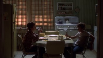 Movie still from “Frailty” (2001), directed by Bill Paxton – Two people sitting at a table in front of an oven; Wide shot, High angle