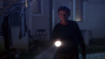 Movie still from “Frailty” (2001), directed by Bill Paxton – A young boy holding a flashlight while standing in a dark room; Medium shot, Low angle