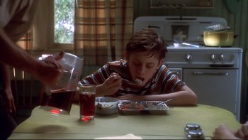 Movie still from “Frailty” (2001), directed by Bill Paxton – A young boy sitting at a table eating food; Medium shot, High angle