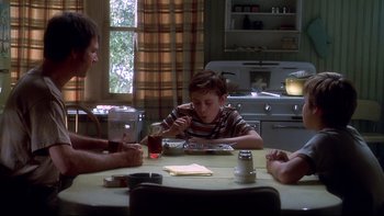 Movie still from “Frailty” (2001), directed by Bill Paxton – A group of people sitting around a table eating; Medium shot, Over the shoulder angle