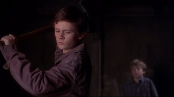 Movie still from “Frailty” (2001), directed by Bill Paxton – A young man holding a baseball bat in a dark room; Medium shot, Over the shoulder angle