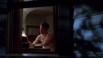 Movie still from “Frailty” (2001), directed by Bill Paxton – A man sitting at a table in front of a laptop computer in front of a mirror; Medium shot, Low angle