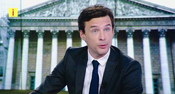 Movie still from “France” (2021), directed by Bruno Dumont – A man wearing a suit and tie sitting in front of a building; Close Up shot, Low angle