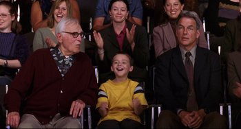 Movie still from “Freaky Friday” (2003), directed by Mark Waters – A group of people sitting in a row with a boy smiling; Medium shot, Over the shoulder angle
