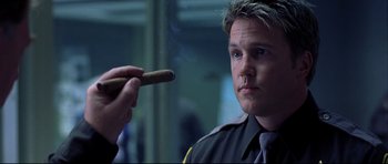 Movie still from “Freddy vs. Jason” (2003), directed by Ronny Yu – A man in a police uniform is looking at a cigar; Close Up shot, Low angle