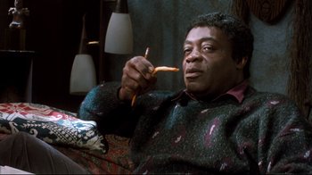 Movie still from “Freddy's Dead: The Final Nightmare” (1991), directed by Rachel Talalay – A man sitting on top of a couch holding a piece of food; Medium shot, High angle