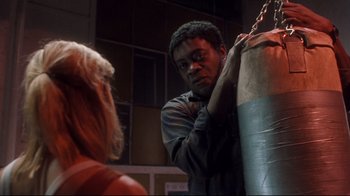 Movie still from “Freddy's Dead: The Final Nightmare” (1991), directed by Rachel Talalay – A man standing next to a woman holding a punching bag; Medium shot, Low angle