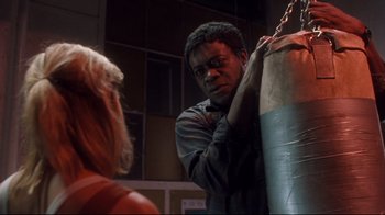 Movie still from “Freddy's Dead: The Final Nightmare” (1991), directed by Rachel Talalay – A man standing next to a woman holding a punching bag; Medium shot, Low angle