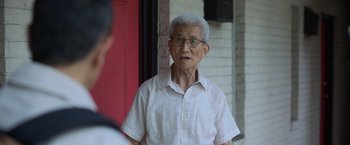 Movie still from “The Valet” (2022), directed by Richard Wong – An older man wearing glasses standing in front of a red door; Close Up shot, Over the shoulder angle