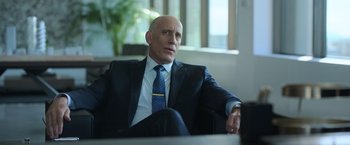 Movie still from “The Valet” (2022), directed by Richard Wong – A man in a suit and tie sitting in a chair; Medium shot, Over the shoulder angle