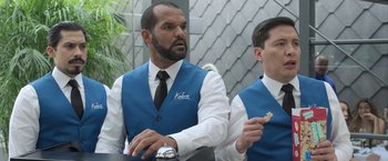 Movie still from “The Valet” (2022), directed by Richard Wong – Two men in blue vests and white shirts are eating; Medium shot, Over the shoulder angle