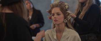 Movie still from “The Valet” (2022), directed by Richard Wong – A woman with curlers in her hair getting ready for a fashion show; Close Up shot, Over the shoulder angle