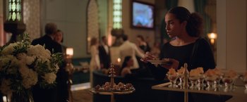 Movie still from “The Valet” (2022), directed by Richard Wong – A woman in a black shirt is serving food; Medium shot, Over the shoulder angle