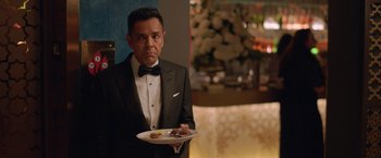 Movie still from “The Valet” (2022), directed by Richard Wong – A man in a tuxedo holding a plate of food; Medium shot, Over the shoulder angle