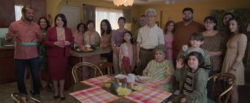 Movie still from “The Valet” (2022), directed by Richard Wong – A group of people standing around a table with food on it; Wide shot, High angle