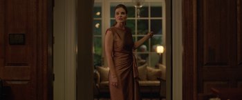 Movie still from “The Valet” (2022), directed by Richard Wong – A woman in a brown dress standing in front of a window; Medium shot, Low angle