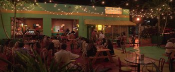 Movie still from “The Valet” (2022), directed by Richard Wong – A group of people sitting at a table in front of a building; Extreme Wide shot, High angle