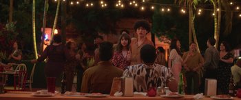 Movie still from “The Valet” (2022), directed by Richard Wong – A group of people sitting at a table with lights in the background; Medium shot, Over the shoulder angle