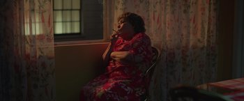 Movie still from “The Valet” (2022), directed by Richard Wong – An older woman sitting in front of a window with a cigarette in her mouth; Medium shot, High angle