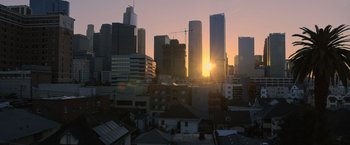Movie still from “The Valet” (2022), directed by Richard Wong – The sun is setting over a city skyline; Extreme Wide shot, High angle