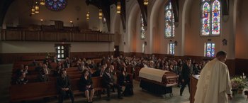 Movie still from “The Valet” (2022), directed by Richard Wong – People sitting in a church with a casket in the background; Extreme Wide shot, High angle
