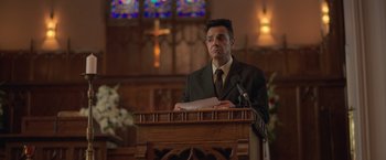 Movie still from “The Valet” (2022), directed by Richard Wong – A man standing at a lectern in front of a microphone; Medium shot, Low angle