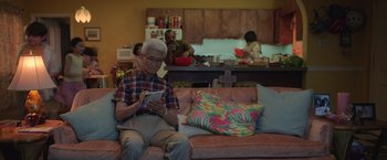 Movie still from “The Valet” (2022), directed by Richard Wong – An older man sitting on a couch looking at his cell phone; Medium shot, Over the shoulder angle