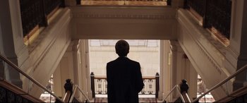 Movie still from “French Exit” (2020), directed by Azazel Jacobs – A man in a suit standing in front of a staircase; Medium shot, Low angle