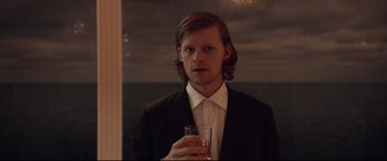 Movie still from “French Exit” (2020), directed by Azazel Jacobs – A man in a suit holding a glass of wine; Close Up shot, Over the shoulder angle