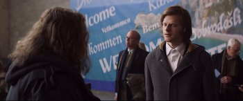 Movie still from “French Exit” (2020), directed by Azazel Jacobs – A group of people standing in front of a welcome sign; Medium shot, Over the shoulder angle