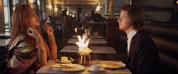 Movie still from “French Exit” (2020), directed by Azazel Jacobs – Two people sitting at a table in front of a lit candle; Medium shot, Over the shoulder angle