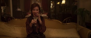 Movie still from “French Exit” (2020), directed by Azazel Jacobs – A woman sitting on top of a couch holding a drink; Medium shot, High angle