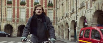 Movie still from “French Exit” (2020), directed by Azazel Jacobs – A man in a gray coat and a scarf is riding a bike; Close Up shot, Low angle