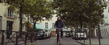 Movie still from “French Exit” (2020), directed by Azazel Jacobs – A woman riding a bike down a street; Wide shot, Low angle