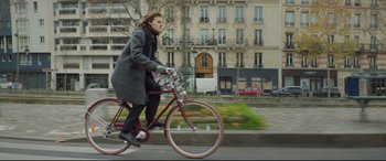 Movie still from “French Exit” (2020), directed by Azazel Jacobs – A man riding a bike down a street; Wide shot, Low angle